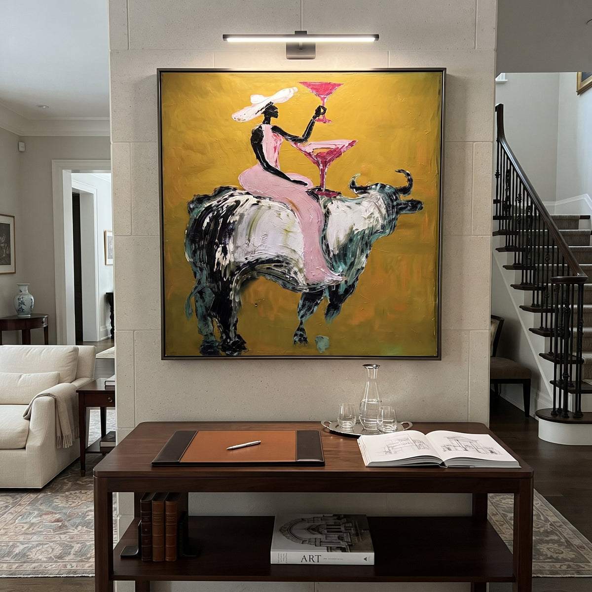 Pink Bull Martini Rider focuses on pink-clad cowgirl on grey bull lifting a martini against mustard ground. The composition is built from the exact pose, clothing shape, accessories, furniture, animal form, shoreline, palm shape, surfboard, or table arrangement visible in this artwork, so the image reads as a specific modern figurative painting rather than a generic decorative abstract. The pink; mustard; grey palette gives the piece its main atmosphere, while smaller dark and light accents